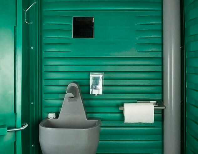 Держатель для полотенец, зеркало и дозатор для мыла в зелёной туалетной кабине «Люкс».
